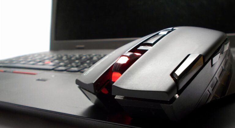 Wireless mouse with red color placed right next to a laptop.