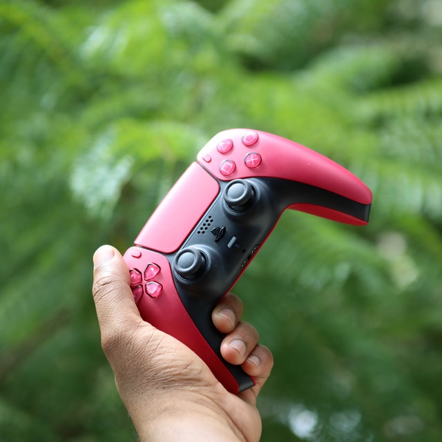 A PS5 controller in red color that look amazing with a green background trees