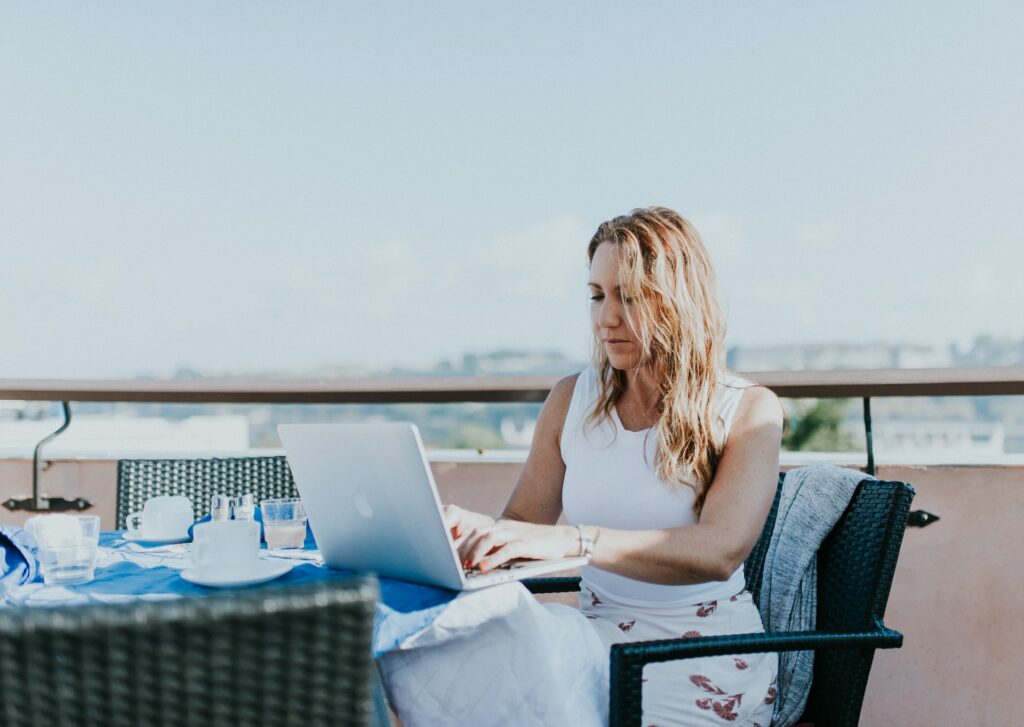 a female digital nomad in white dress working on her laptop on the roof in a beautiful atmosphere