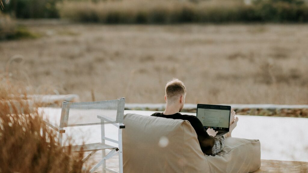 a digital nomad with a laptop on his thigs sitting on a beach.